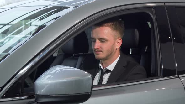 Cheerful Businessman Holding Car Keys Sitting in a New Auto at the Dealership alt