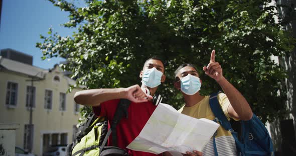 Two mixed race male friends wearing face masks using map in the street alt