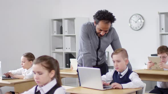 Afro-American Teacher Checking on Pupils at Computer Class alt