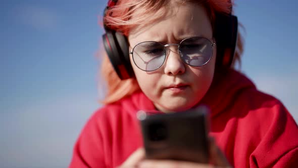 Chubby Child Girl is Playing Video Game in Smartphone Listening to Music By Headphones alt