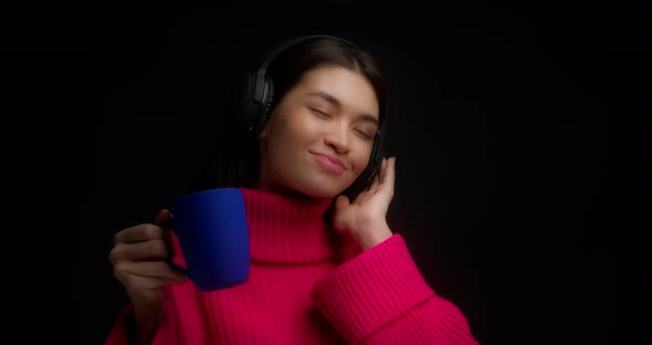 Cute Woman Enjoy Music with Wireless Headphones and Drinks From a Blue Mug