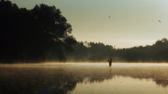Fisherman pulling fish on the river in a foggy summer morning. Fishing for spinning. alt