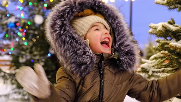 Portrait of happy girl in winter in fur hood against background of fairy lights, Christmas trees alt