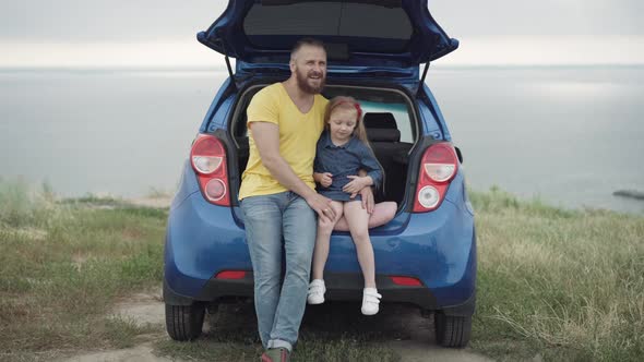 Wide Shot of Carefree Happy Loving Father and Daughter Sitting in Car Trunk Talking Smiling Pointing alt