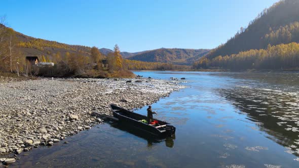 Man Throws a Fishing Rod on the Bank of a Beautiful Wide River Boat Mountain Autumn alt