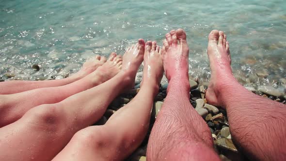 These are the Bare Feet of a Family in the Sea Waves on a Stone Shore