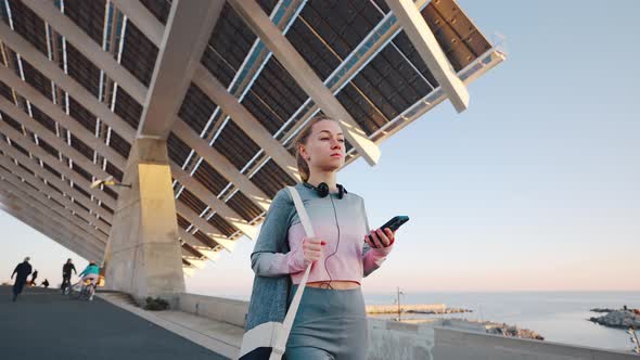 Millennial Female Marching Alone Embankment After Jogging Looking on Phone alt
