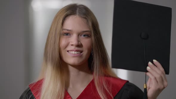 Closeup Mortarboard with Cheerful Young Woman Emerging and Hiding Looking at Camera alt