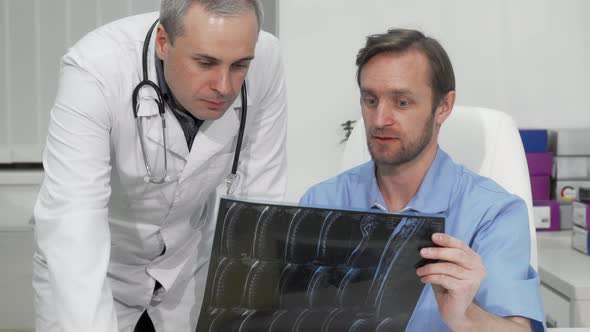 Mature Male Surgeon Asking Advice of His Colleague on MRI Scan of the Patient