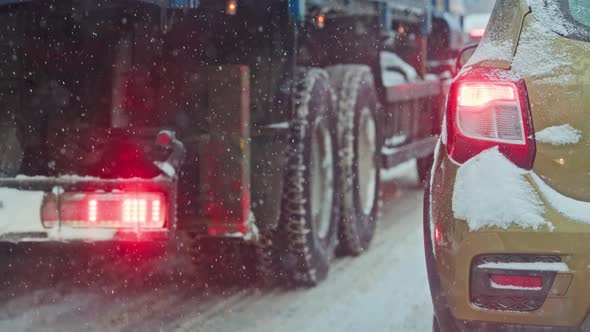 Snow Covered Car Tail Light at Winter Day Near Truck During Snowfall alt