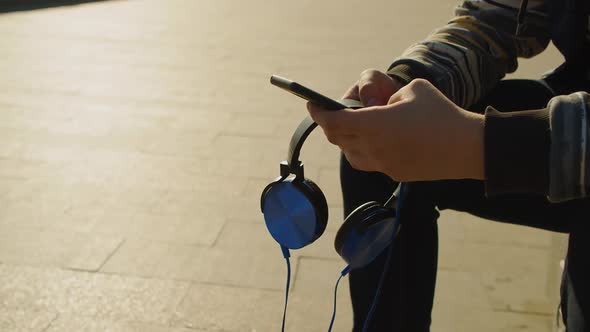 Hands of a Teenage Boy with Smartphone and Headphones  He Chatting with Friends Outdoor alt