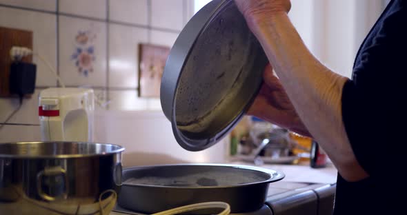 A woman chef coating round baking pans with flour to prevent sticking as she bakes vegan chocolate c alt