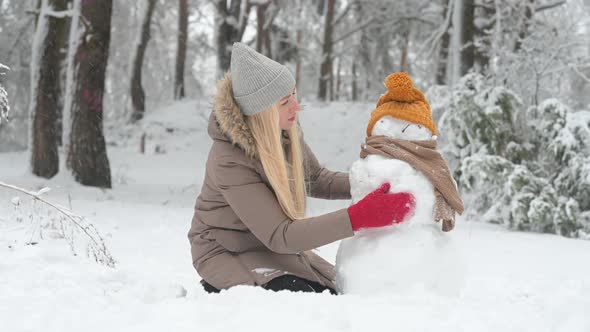young girl is building a snowman in a snowy park