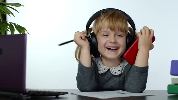 Child Schoolgirl Laughing and Smiling. Learning Lessons at Home and Using Digital Smartphone alt