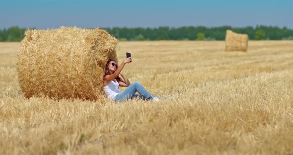 Cute Girl in Sunglasses is Photographed By a Large Haystack in a Wheat Field alt