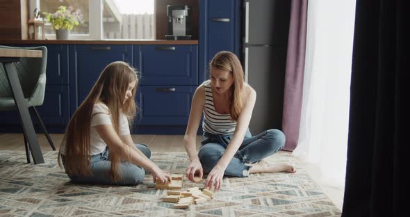 Mother and Daughter Build Tower From Wooden Bricks Sitting on a Floor at Home alt