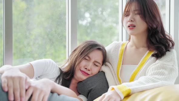 Asian woman comforts her crying friend on the sofa in the living room alt