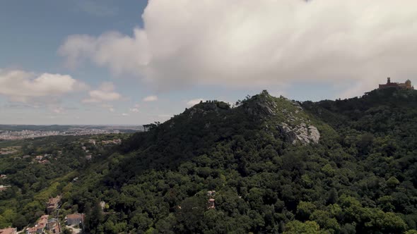 Aerial panning shot of Sintra Hills against beautiful cloudscape and Pena palace alt
