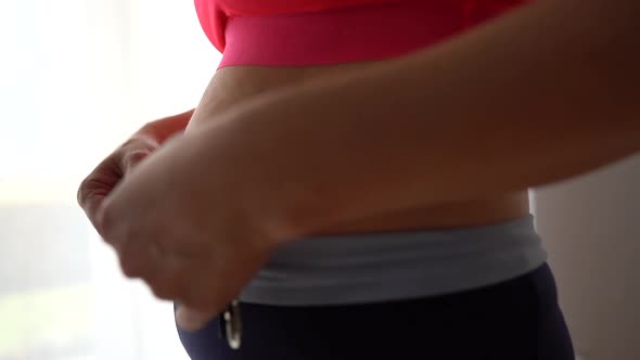 Closeup of a Pregnant Woman in a Red Sports Top and Leggings Measuring Her Waist with a Tape Measure alt