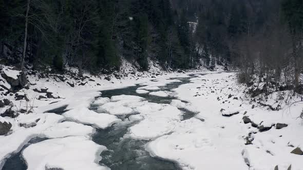 Aerial View in Winter on a Mountain River with a Forest During a Snowfall alt