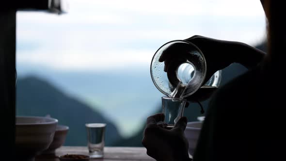 Closeup of a hand pouring drip coffee into a glass with blurred nature background