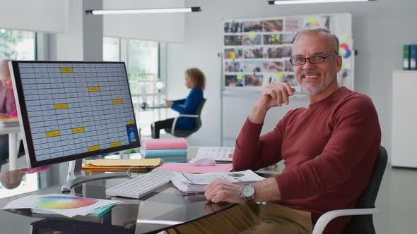 Portrait of Smiling Senior Businessman Sitting at Desk in Modern Office and Smiling at Camera alt