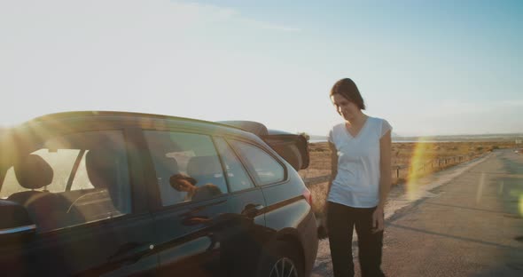 Girl in sunlight closing the boot of car and gets behind wheel to continue trip alt