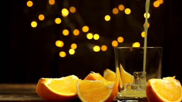 A Few Slices Of Orange And Juice Are Poured Into A Glass With Lights In The Background Close