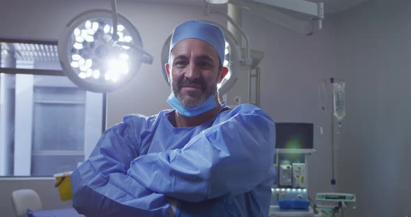 Portrait of caucasian male surgeon wearing lowered face mask smiling in operating theatre alt
