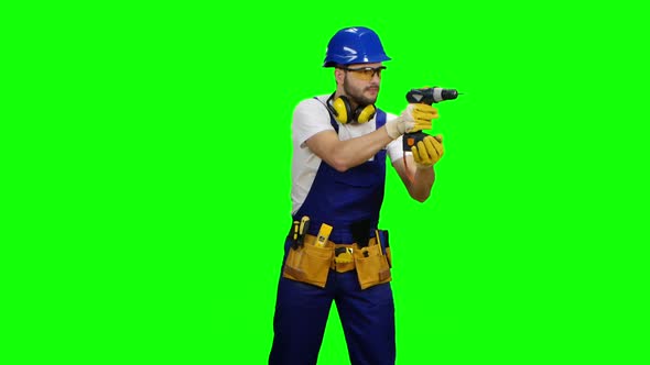 Builder Holds a Drill in His Hands and Looks Around. Green Screen alt