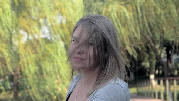 Portrait of a Beautiful Blonde Girl with Waving Hair Looking at Camera in the Park on Sunny Day