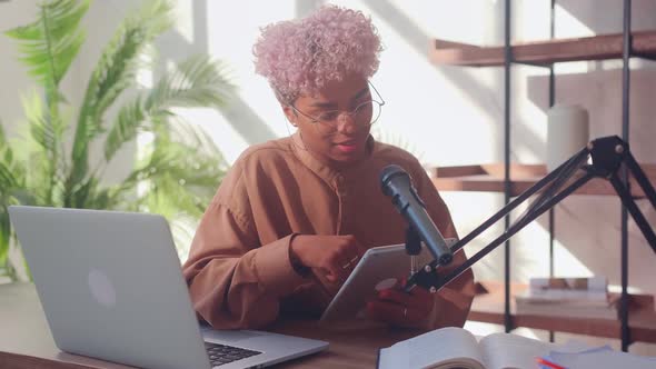 Woman in Front of a Microphone Reads on a Digital Tablet During a Podcast alt
