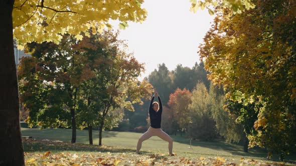 Young Woman Practices Goddess Yoga Pose in Autumn City Park on a Yoga Mat
