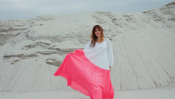 Model Woman in Dress Walking on the Sand Smiling at Camera Stones in the Background alt