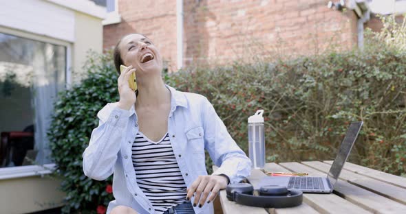 Woman sitting in garden and laughing on the phone