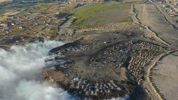 Burning garbage pile in trash landfill polluting city with smoke alt