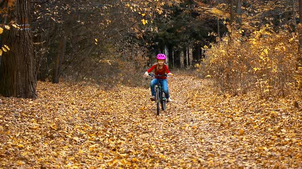 A little girl rides a bike in the autumn Park and falls.