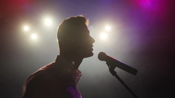Man Stand Up Comedian Telling Funny Jokes in Micropphone Standing on Stage.