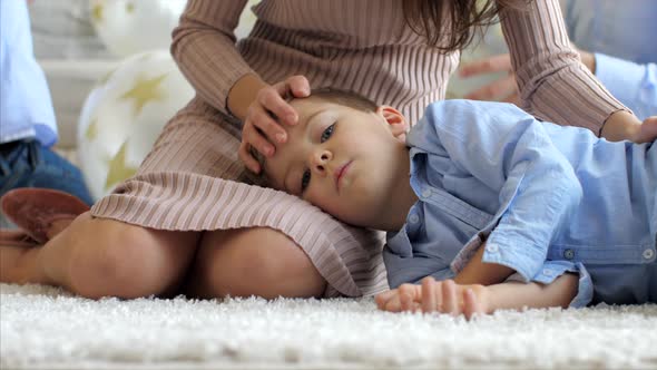 Little Son Is Lying on Mother's Knees on the Floor While Mom Is Stroking Him