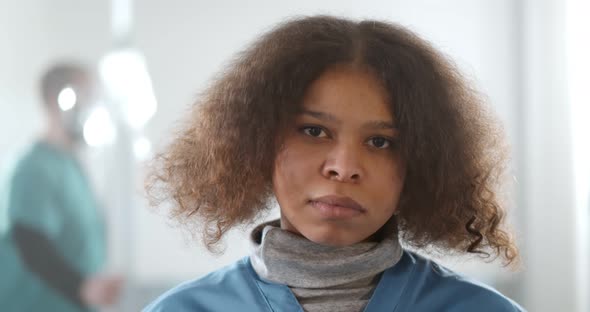 Portrait of Young Tired Afroamerican Female Doctor Looking at Camera in Hospital Corridor alt
