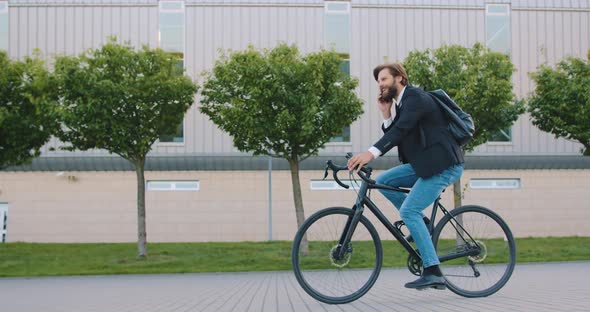 Bearded Man in Stylish Clothes Which Riding a Bike and Has Positive Phone Conversation alt