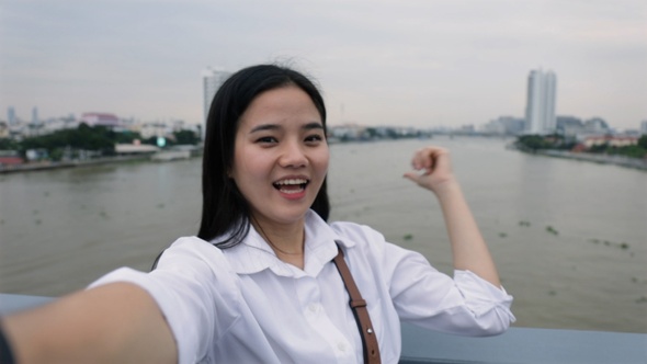 Asian female video chatting with her friends while standing on the Rama VIII Bridge in Thailand.