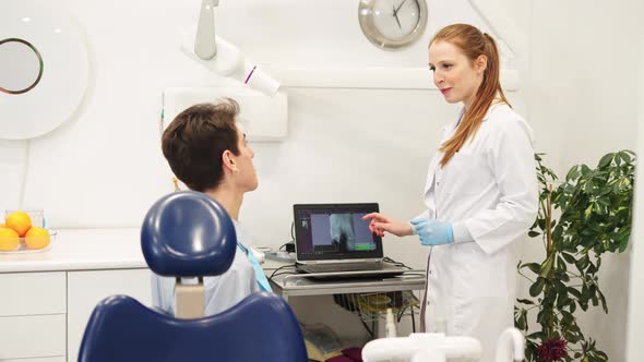 Female Dentist Showing Dental Xray on Computer and Explaining Diagnose to Male Patient alt