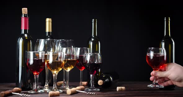 A Man's Hand Puts a Glass of Wine on the Table. On a Black Background alt