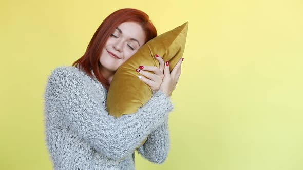 Smiling Red Haired Woman in Sweater Embracing Pillow, Posing on Yellow Background