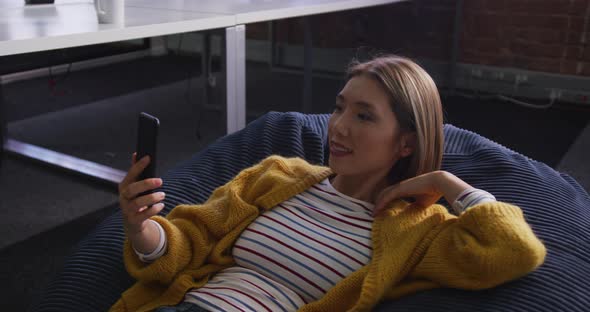 Asian business woman lying on bean bag taking selfie and smiling during break alt