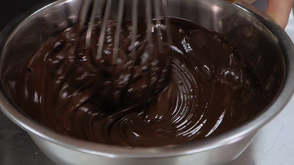 Closeup of a Pastry Chef Mixing Liquid Chocolate with a Whisk in a Bowl alt