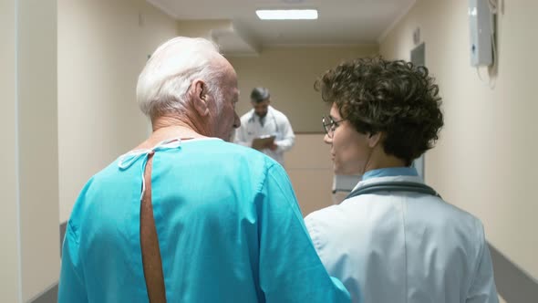 Female doctor accompanying old patient through corridor