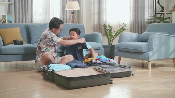 Dad And Son Packing Clothes In Suitcase At Home, Preparing For Their Vacation alt