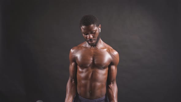 A Darkskinned Man Lifts a Barbell on an Isolated Dark Background